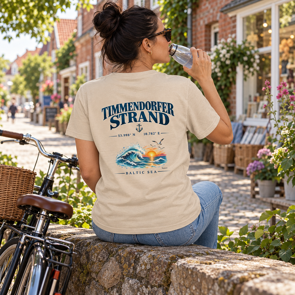 Frau im Essential-T-Shirt in Natural mit Baltic Sea Backprint bei einer Fahrradausflugspause in einer Küstenstraße.