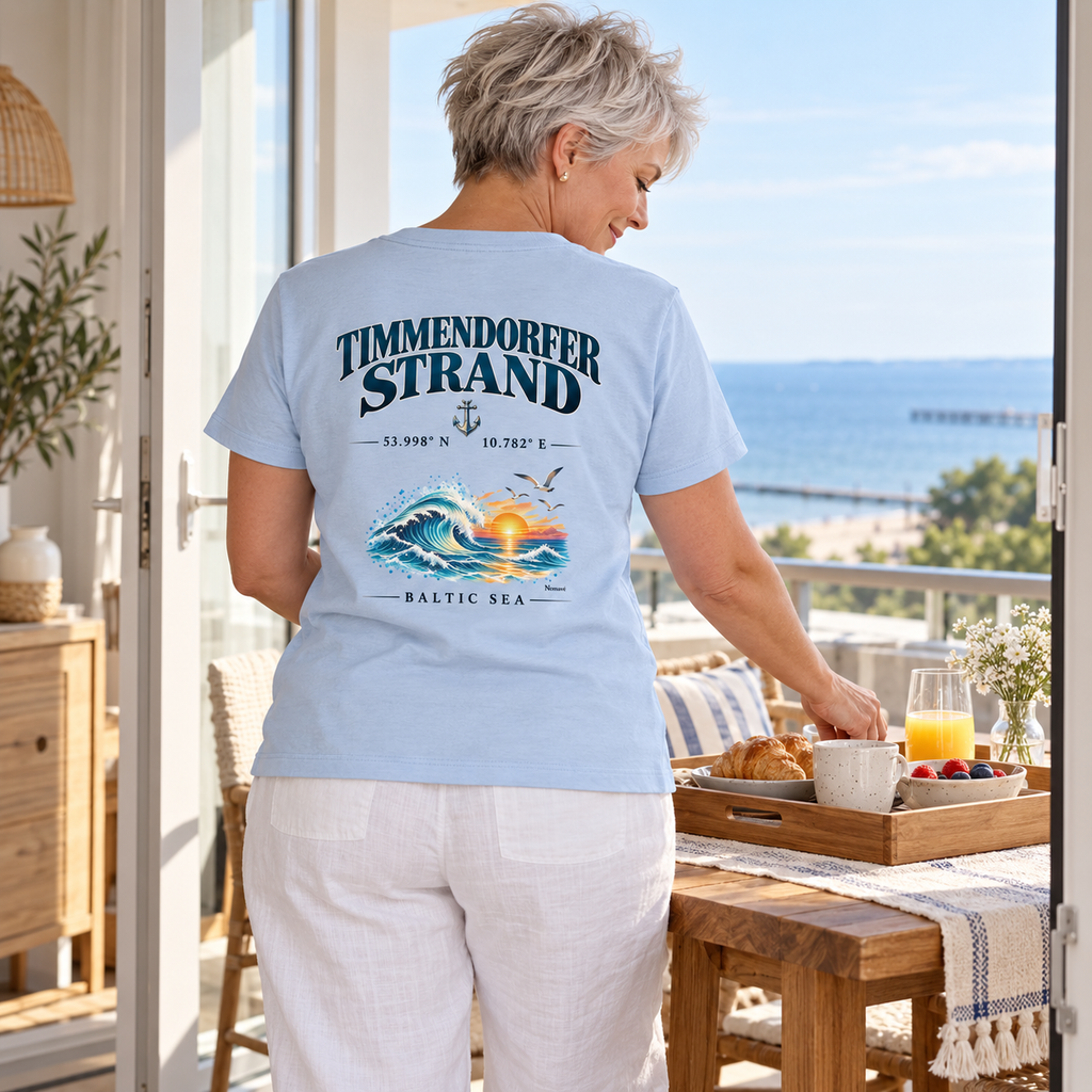 Frau im Damen Bio-T-Shirt in Blue Soul mit Timmendorfer Strand – Baltic Sea Rückenprint beim Frühstücksvorbereiten in einer Ferienwohnung.