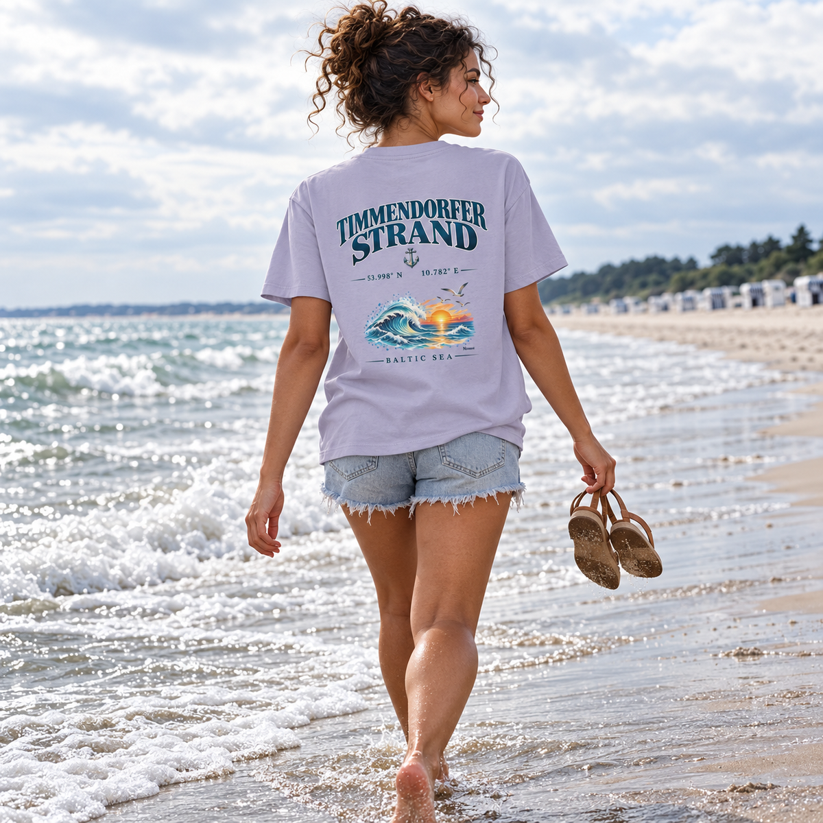 Frau im Damen Bio-T-Shirt in Lavender mit Baltic Sea Backprint beim barfüßigen Spaziergang an der Ostsee.