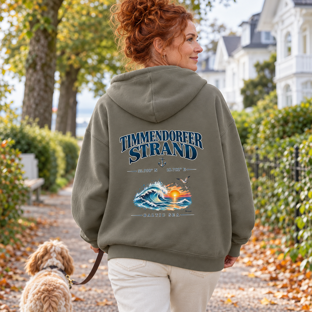 Frau im Bio-Oversize-Hoodie in Khaki mit Baltic Sea Backprint beim Hundespaziergang durch einen Küstenort.