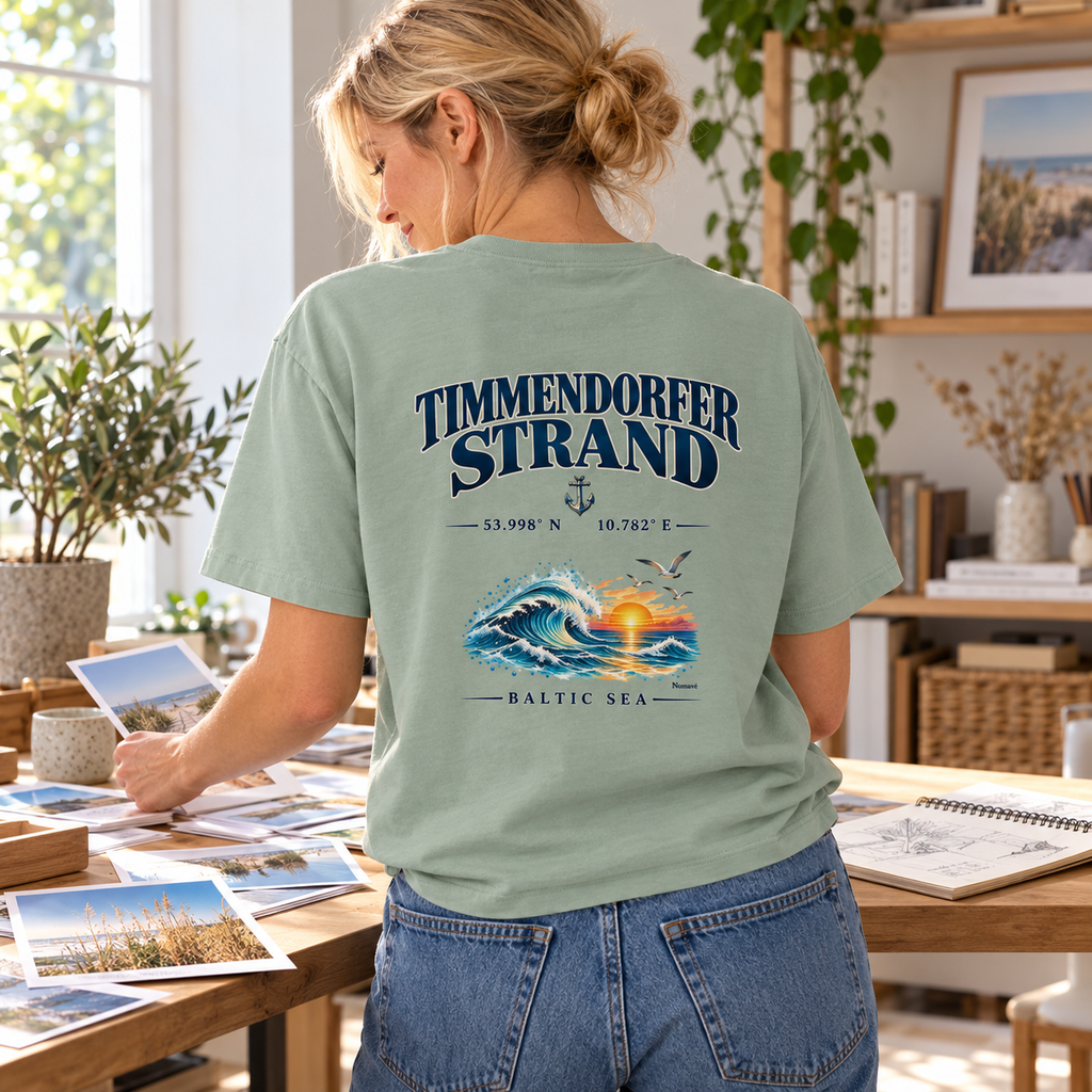 Frau im Bio-Heavy-T-Shirt in Aloe mit Baltic Sea Backprint beim Sortieren von Urlaubsfotos am kreativen Arbeitsplatz.