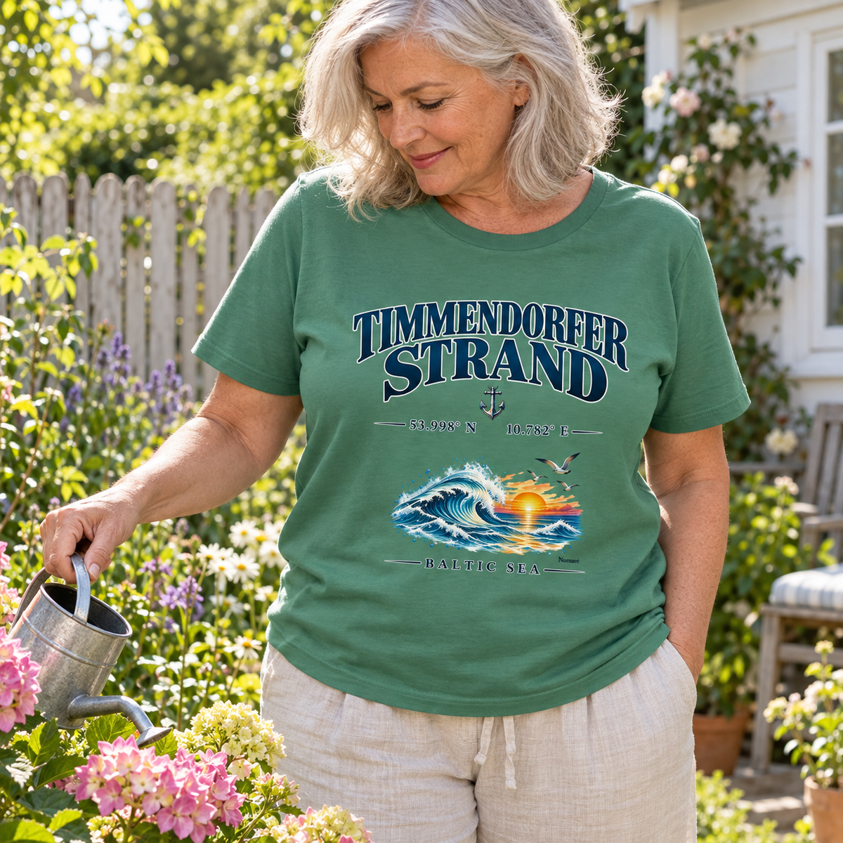 Frau im Unisex Bio-T-Shirt in Green Bay mit Baltic Sea Frontprint beim Blumengießen im Garten.
