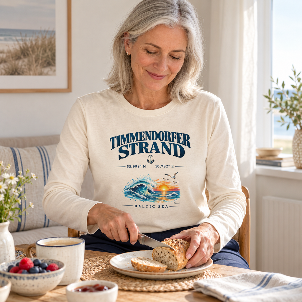 Frau im Unisex Bio-Longsleeve in Natural Raw mit Timmendorfer Strand – Baltic Sea Frontprint beim Frühstück in einer Ferienwohnung.