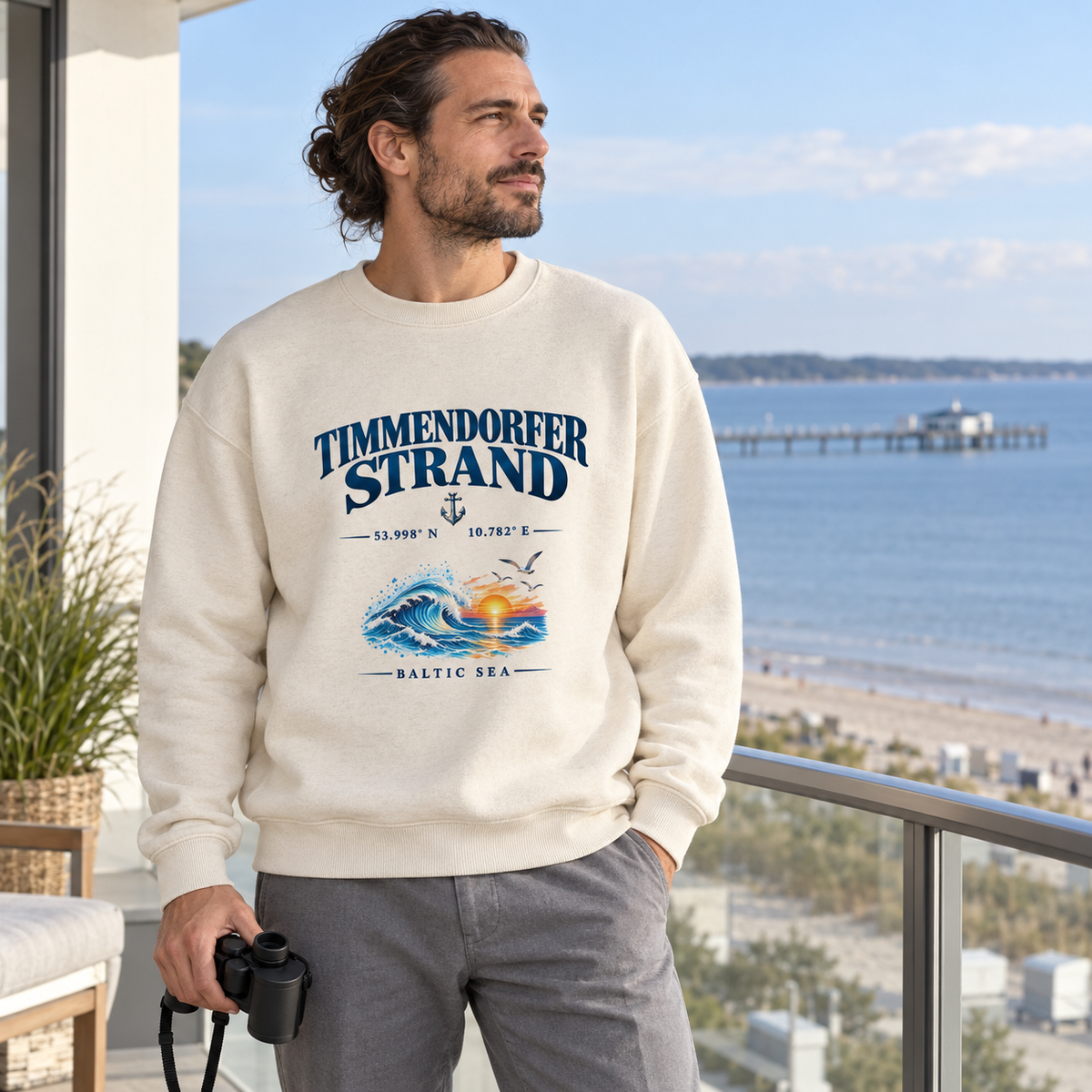Unisex Bio-Oversize-Sweatshirt in Natural Raw mit Timmendorfer-Strand–Baltic-Sea-Frontmotiv: Mann mit Fernglas auf einem Balkon am Meer.