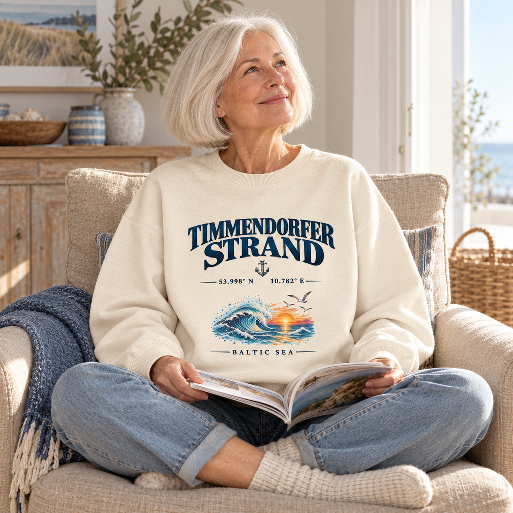 Unisex Bio-Oversize-Sweatshirt in Cream mit Timmendorfer-Strand–Baltic-Sea-Frontmotiv: ältere Frau liest eine Zeitschrift im Sessel einer hellen Ferienwohnung.