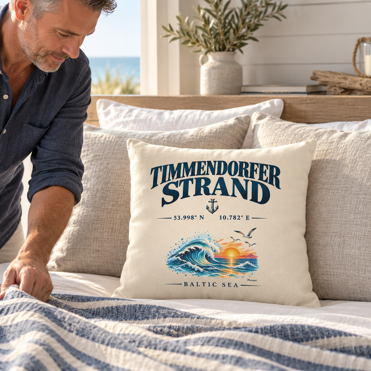 Kissen Natur 40 × 40 cm mit Timmendorfer-Strand–Baltic-Sea-Motiv auf der Vorderseite: Kissen steht vor Leinenkissen auf einem Bett, während ein Mann die Decke richtet.