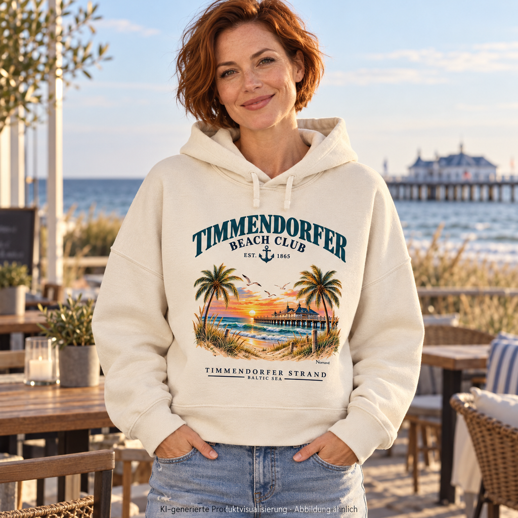 KI-generierte Produktvisualisierung: Frau vor einem Küstencafé im Timmendorfer Beach Club Damen Bio-Boxcut-Hoodie in Natural Raw mit maritimem Frontprint.