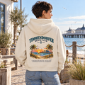 KI-generierte Produktvisualisierung: Frau im Damen Bio-Boxcut-Hoodie Natural Raw mit Timmendorfer-Beach-Club-Rückendruck in einem maritimen Hof.
