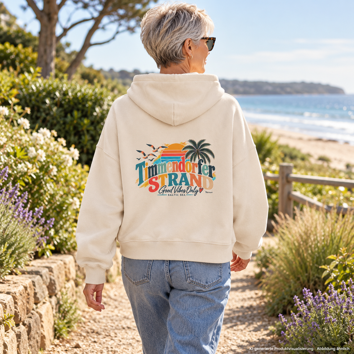KI-generierte Produktvisualisierung: Frau im Natural-Raw-Boxcut-Hoodie mit Good-Vibes-Only-Rückenprint auf einem Küstengartenweg.