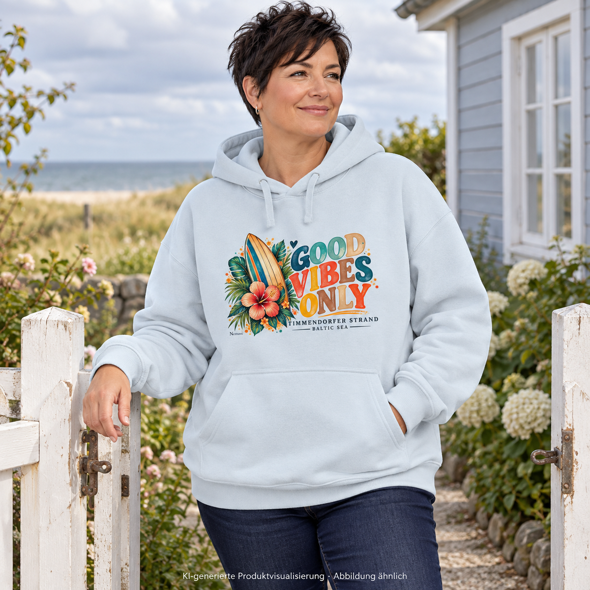 KI-generierte Produktvisualisierung: Frau im Bio-Oversize-Hoodie in Blue Ice mit Surfboard-, Hibiskus- und Good-Vibes-Only-Frontprint am Gartentor eines Ferienhauses am Meer.