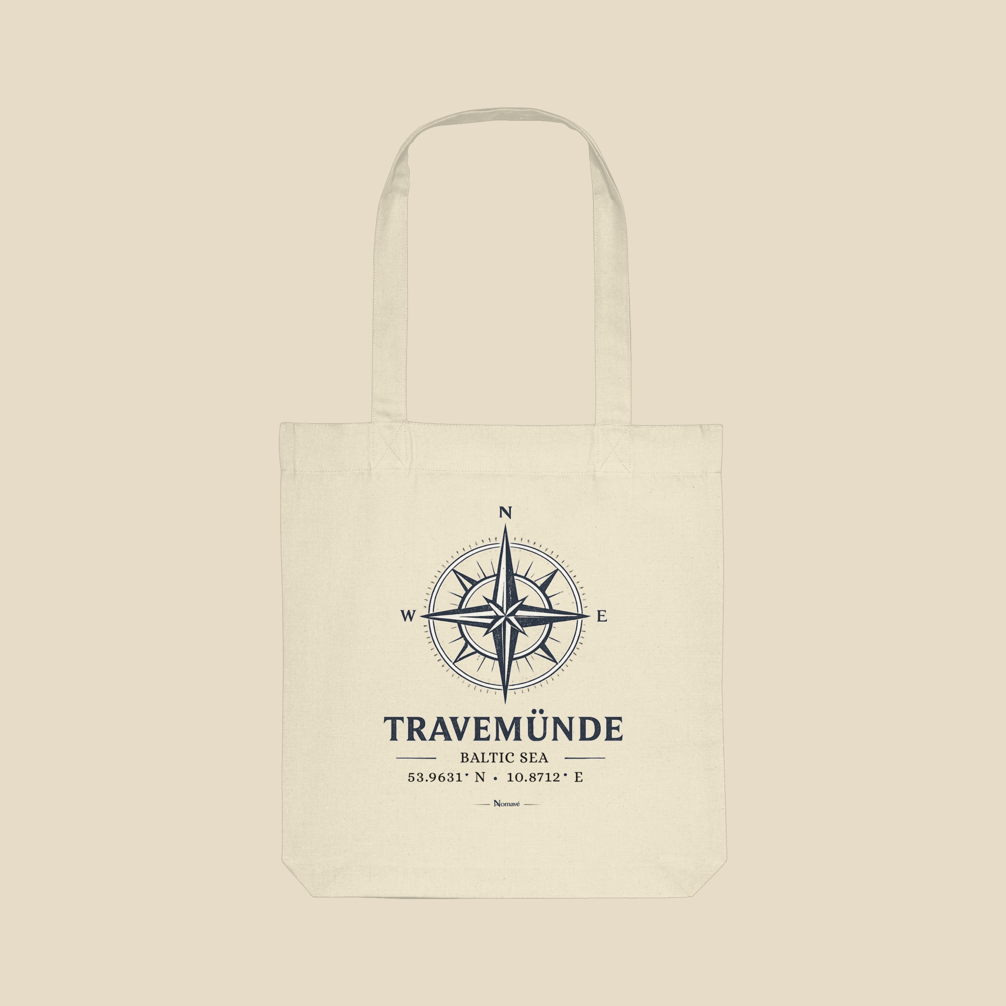 Cremefarbene Nomavé Bio-Stofftasche mit „Travemünde Baltic Sea“-Kompassmotiv im cleanen Produktmockup. Nachhaltige Baumwolltasche für Alltag, Strand und Ostsee-Ausflüge.