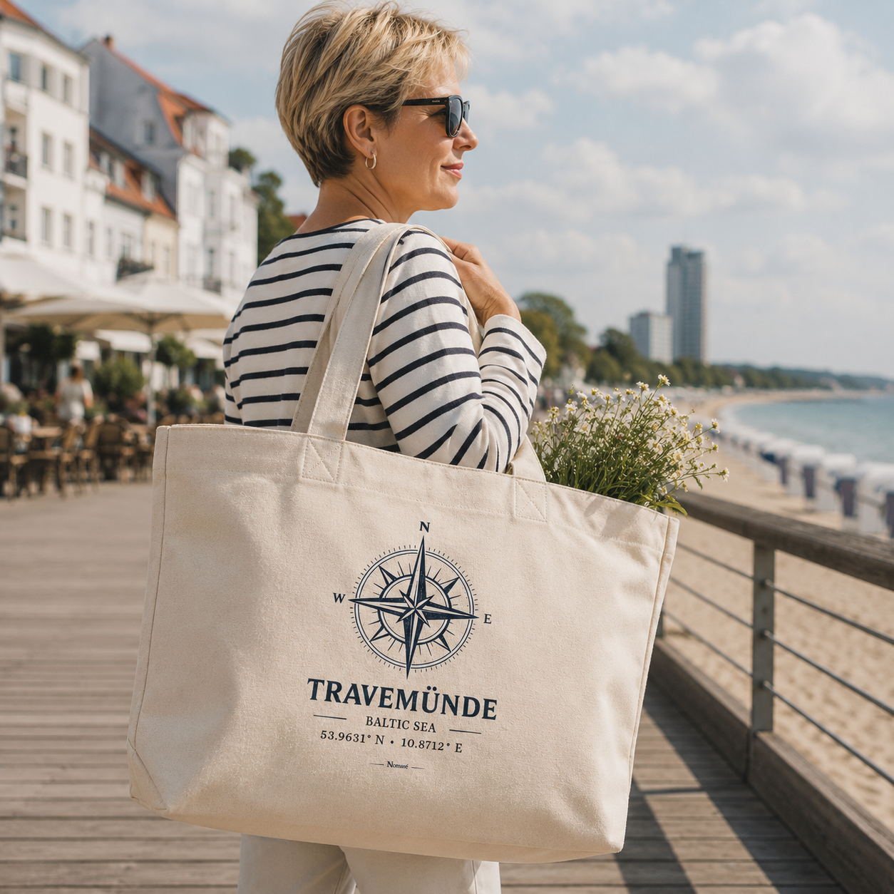 Frau mit nachhaltiger Nomavé Bio-Strandtasche mit „Travemünde Baltic Sea“-Kompassmotiv an der Vorderreihe in Travemünde. Die geräumige Tasche aus Bio-Baumwolle wird entspannt über der Schulter getragen und eignet sich ideal für Strand, Einkäufe, Freizeit, Reisen und den Ostseeurlaub.
