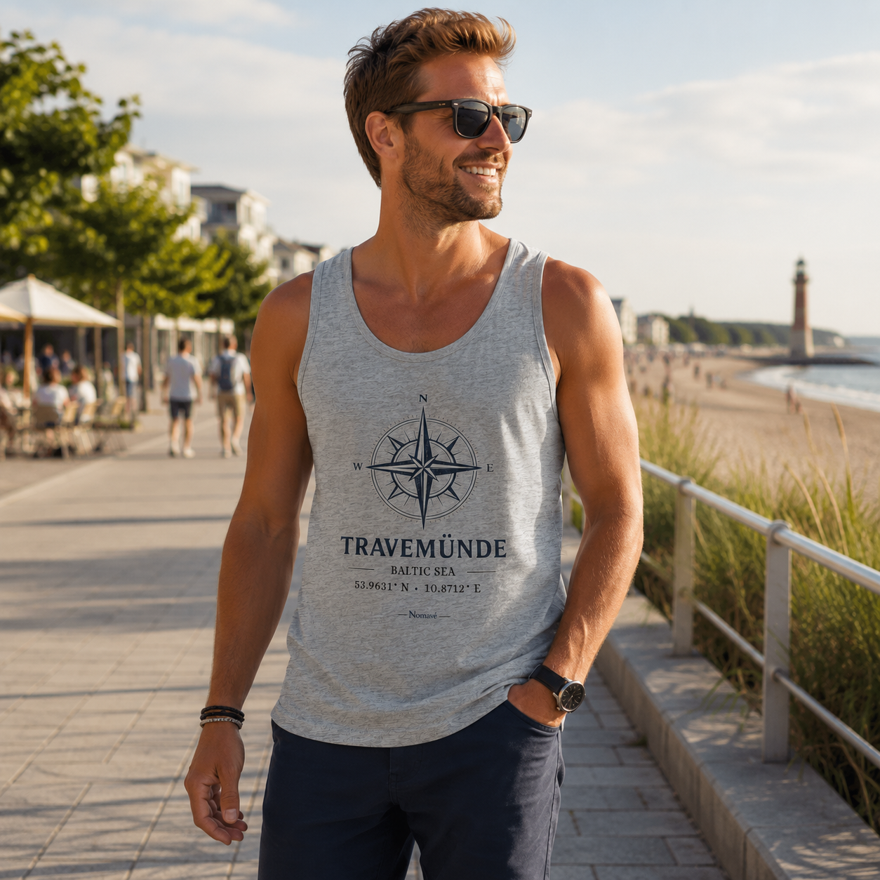 Mann trägt ein hellgraues Bio-Tanktop mit maritimem Kompassmotiv „Travemünde Baltic Sea“ von Nomavé und spaziert bei warmem Morgenlicht über die Strandpromenade an der Ostsee. Mit Sonnenbrille und sommerlichem Outfit vermittelt das Tanktop entspanntes Küstengefühl und eignet sich ideal für Strandtage, Urlaub, Freizeit und Spaziergänge entlang der Ostseeküste.