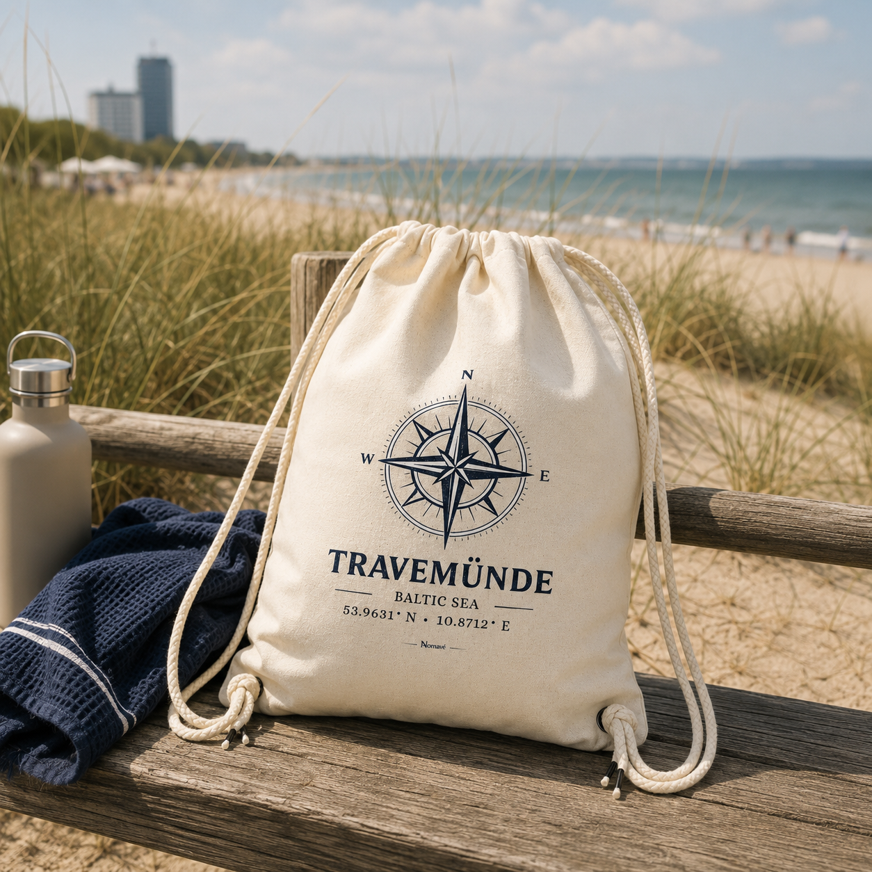Nachhaltiger Nomavé Bio-Turnbeutel mit „Travemünde Baltic Sea“-Kompassmotiv am Ostseestrand in Travemünde. Der Baumwollbeutel steht mit Trinkflasche und Strandtuch auf einer Holzbank und ist der ideale Begleiter für Strand, Freizeit, Sport, Ausflüge und den Ostseeurlaub.