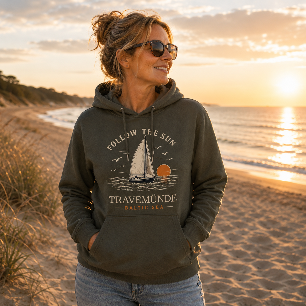 Frau trägt Travemünde Follow The Sun Dark Edition Hoodie am Strand bei Sonnenuntergang
