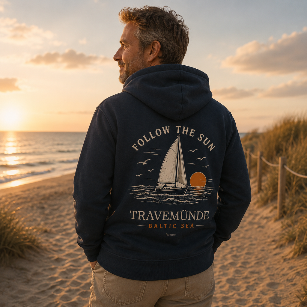 Mann trägt dunkelblauen Travemünde Follow the Sun Hoodie mit großem Rückenprint am Ostseestrand bei Sonnenuntergang