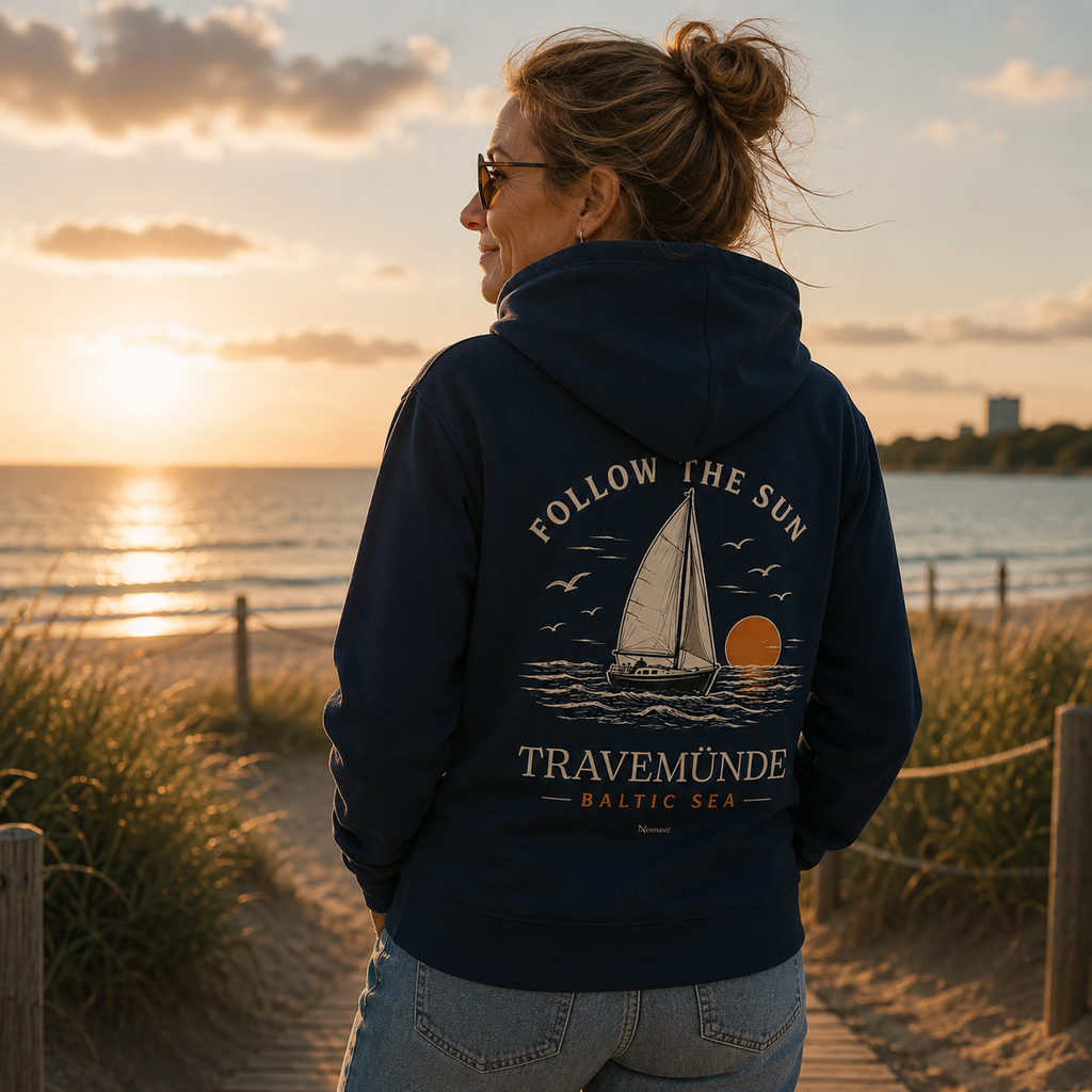 Frau trägt dunkelblauen Travemünde Follow the Sun Hoodie mit großem Rückenprint und blickt bei Sonnenuntergang auf die Ostsee